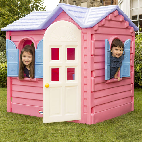 Pink playhouse with two children peeking out of windows on a grassy area.