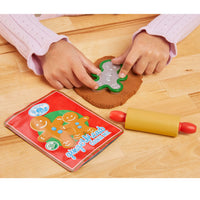 Load image into Gallery viewer, Child's hands using a gingerbread man cookie cutter on dough with a cookie book and rolling pin on a wooden table.
