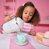 Load image into Gallery viewer, A young girl with curly hair pours milk from a retro-style white electric kettle with chrome accents into a mint green teacup on a saucer, set in a pink-themed room with cupcakes on the table.