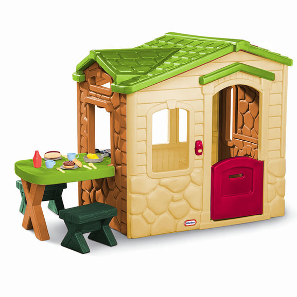 Children's playhouse with a green roof and red door, accompanied by a small table and chairs on a white background.