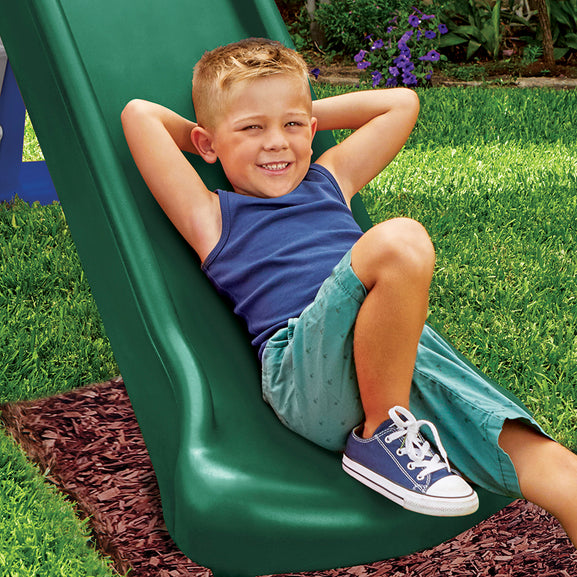 Child sitting on a green slide in a grassy area