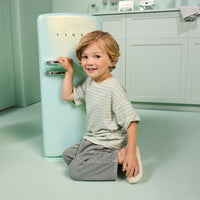 Load image into Gallery viewer, A young child with blonde hair kneels on the floor next to a retro-style mint green refrigerator in a matching pastel kitchen setting. The refrigerator has the brand name 'TIKE' visible on the front.
