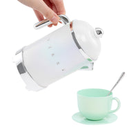 Load image into Gallery viewer, A hand holds a white electric kettle with silver accents, pouring hot water into a mint green ceramic cup and saucer with a spoon, set against a solid white background.
