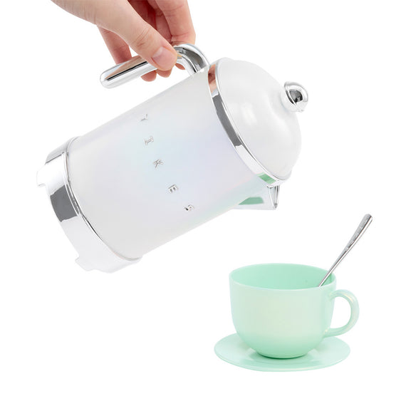 A hand holds a white electric kettle with silver accents, pouring hot water into a mint green ceramic cup and saucer with a spoon, set against a solid white background.