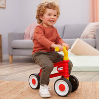 Load image into Gallery viewer, Child sitting on a red and yellow toy tricycle in a living room.
