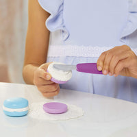 Load image into Gallery viewer, Child&#39;s hands using a purple spatula to frost toy macarons 
