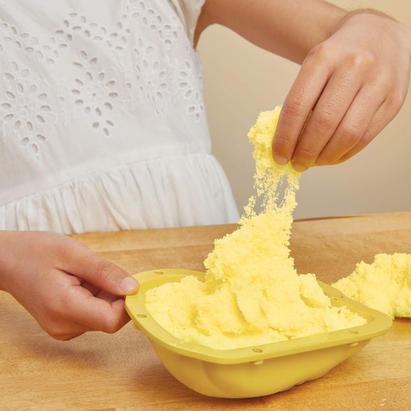 Child playing with yellow play dough on a wooden table