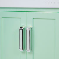Load image into Gallery viewer, Close-up of mint green cabinet doors with polished silver vertical bar handles, with a small portion of a white countertop visible at the top.
