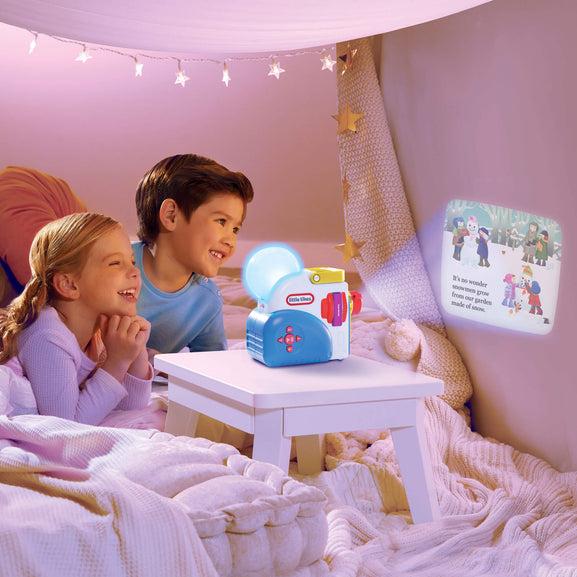 Children in bed with a night light and book, surrounded by cozy bedding and string lights.