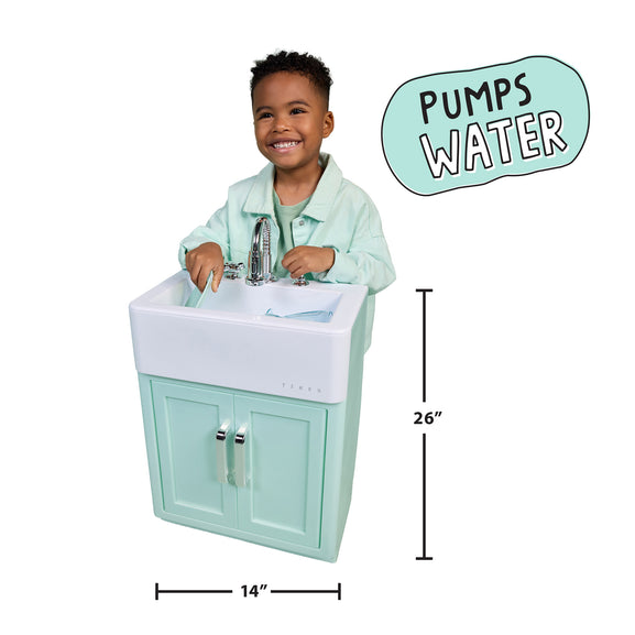 A child sitting behind a small mint green and white vanity sink with a faucet, shown on a white background with dimension lines indicating 14 inches wide by 26 inches tall, plus a badge that says 'PUMPS WATER'.